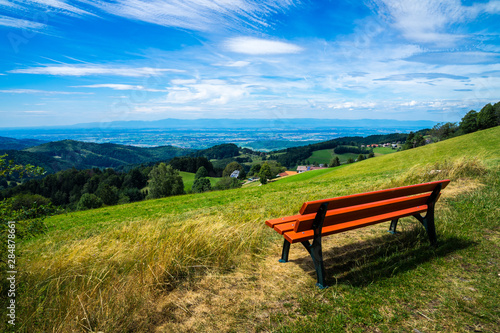 Germany, Orange wooden bench on top of a mountain with fantastic view over endless valley and black forest nature landscape