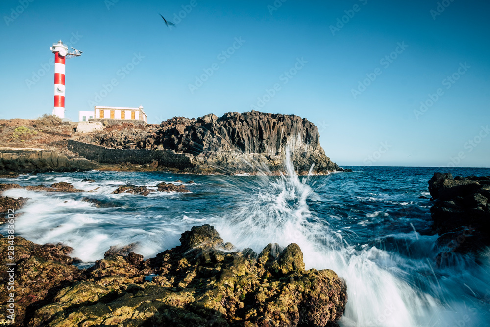 Beautiful scenic landscape with classic lighthouse on the coast and blue ocen and sky in background - concept of travel and vacation for tourism - wave and rocks - obrazy, fototapety, plakaty 