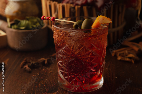 cocktail in rox decorated with black olives on a wooden background. Background decorated with fruits and herbs. photo