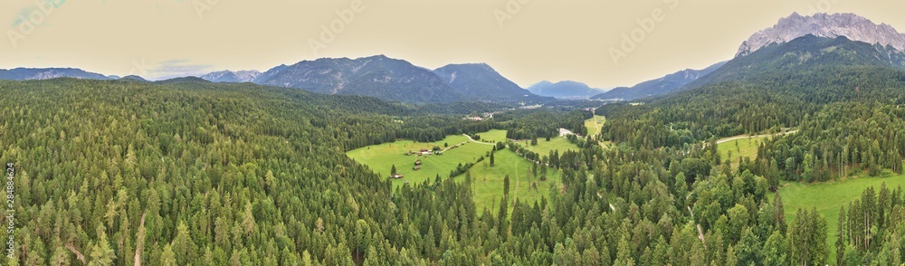 Panorama of a forest and a valley with meadows and pastures in front of the mountains of the Alps, composed of several aerial photos, high resolution
