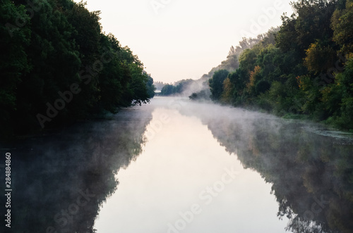 Fog above the water. Trees in the fog next to the river. River at dawn in the summer