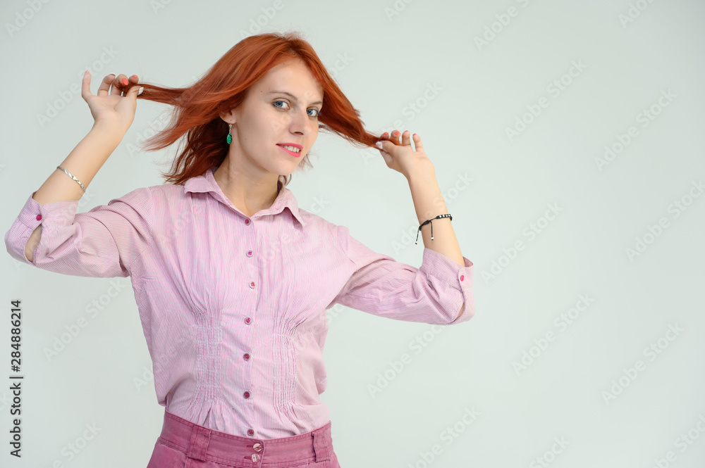 Photo Portrait of a cute girl woman with bright red hair manager in a pink shirt on a white background in studio. He talks, shows his hands in front of the camera with emotions. Photo Portrait of a cute girl woman with bright red hair manager in a pink shirt on a white background in studio. He talks, shows his hands in front of the camera with emotions.