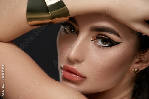 luxury golden and black make-up on brunette face with golden jewelry photo