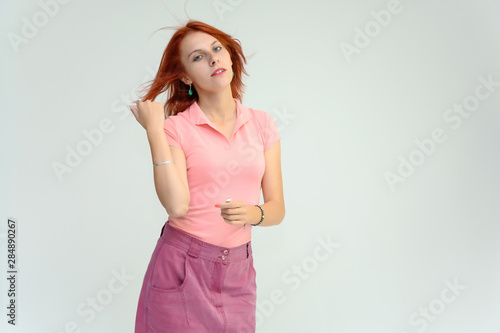 Photo Portrait of a cute woman girl with bright red hair in a peach t-shirt and pink skirt on a white background in studio. He talks  shows his hands in front of the camera with emotions.