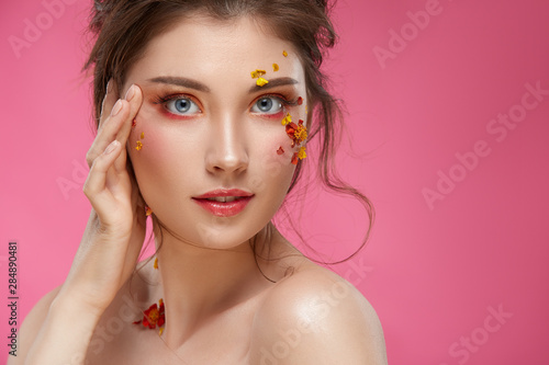 pretty girl with colorful mua and fresh flowers on her face isolated on pink