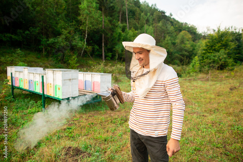 A beekeeper in a protective cap prepares a tool for smoking bees from a hive in the apiary. Smoke for bees, equipment on apiary