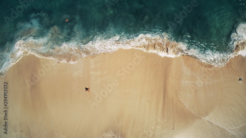 Aerial Top Drone View on Ocean Waves and White Sand Beach. Crystal Water Landscape in Tropical Bali Island, Indonesia. People Walk, Swim and Relax. Cinematic Filter Toning