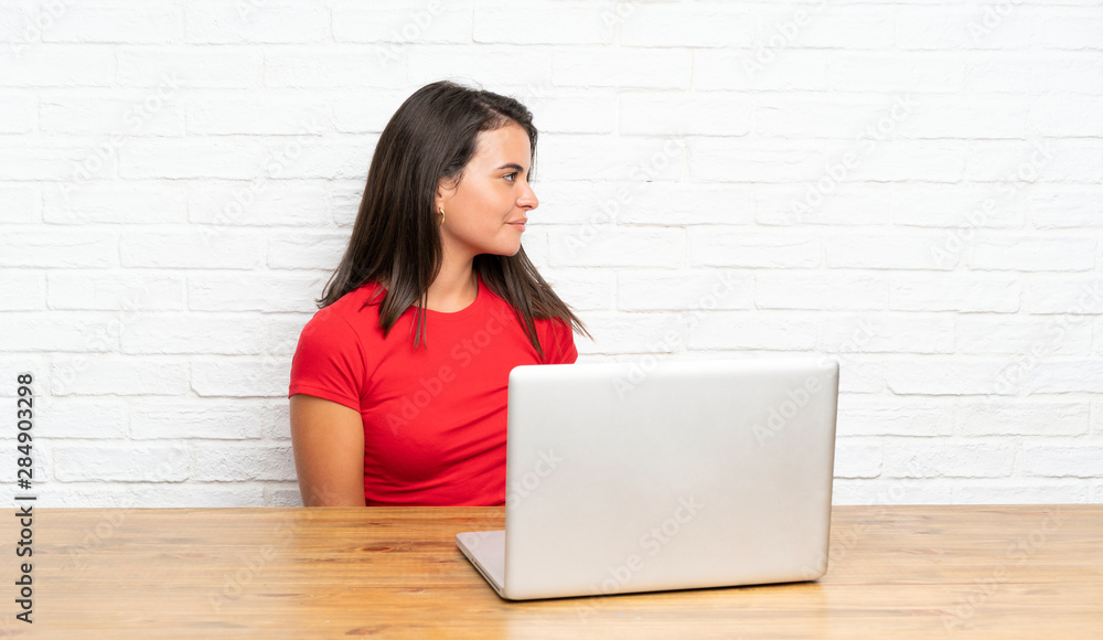 Young girl with pc in a table looking to the side Young girl with pc in a table looking to the side