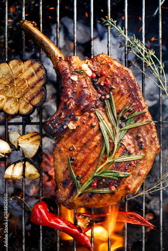Grilled bone-in pork chop, pork steak, tomahawk in a rosemary-garlic marinade  on a flaming grill plate, close-up, top view. Barbecue, bbq meat