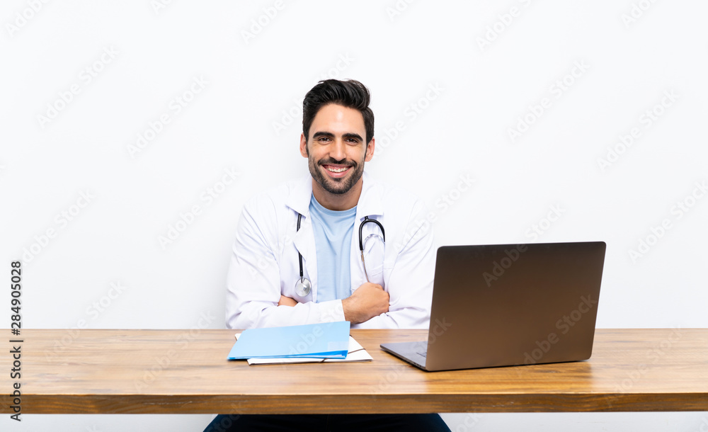 Young doctor man with his laptop over isolated wall laughing Young doctor man with his laptop over isolated wall laughing