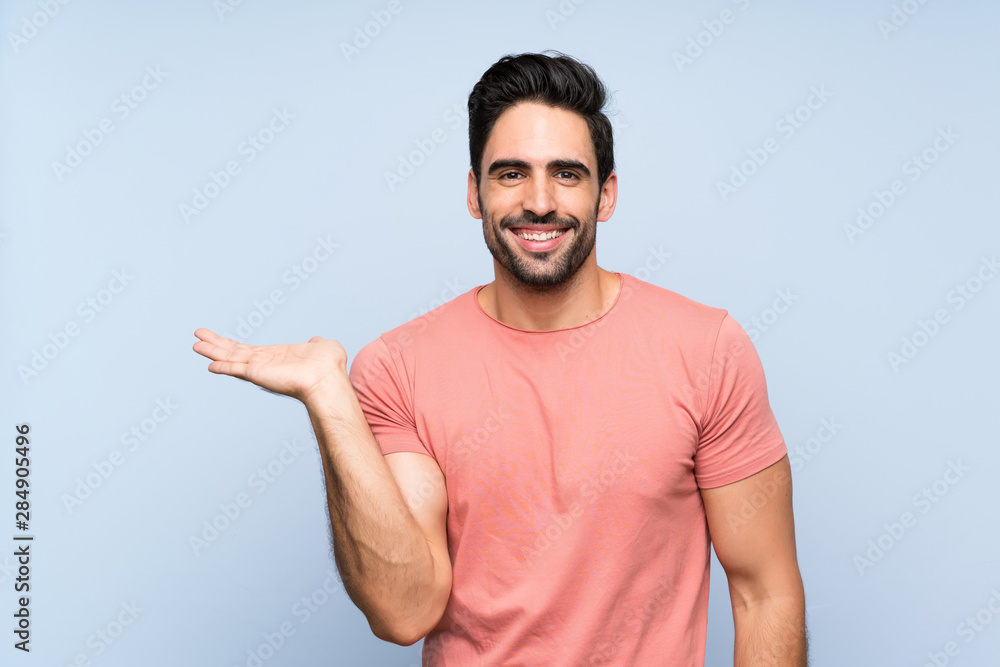 Fototapeta premium Handsome young man in pink shirt over isolated blue background holding copyspace imaginary on the palm to insert an ad