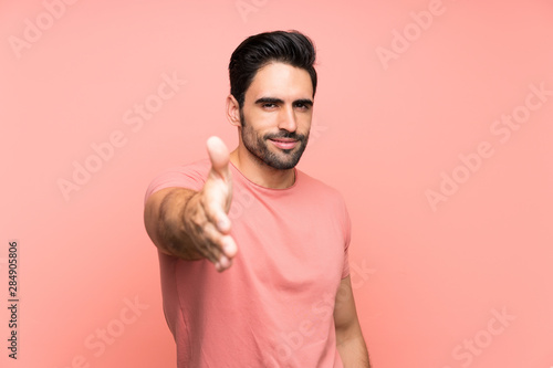 Handsome young man over isolated pink background handshaking after good deal