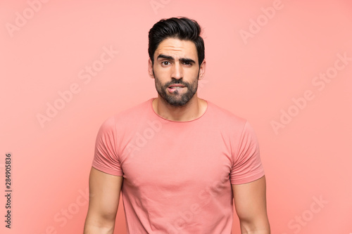 Handsome young man over isolated pink background having doubts and with confuse face expression