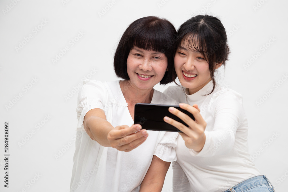 Happy Asian senior woman and daughter taking selfie together isolated on white background Happy Asian senior woman and daughter taking selfie together isolated on white background