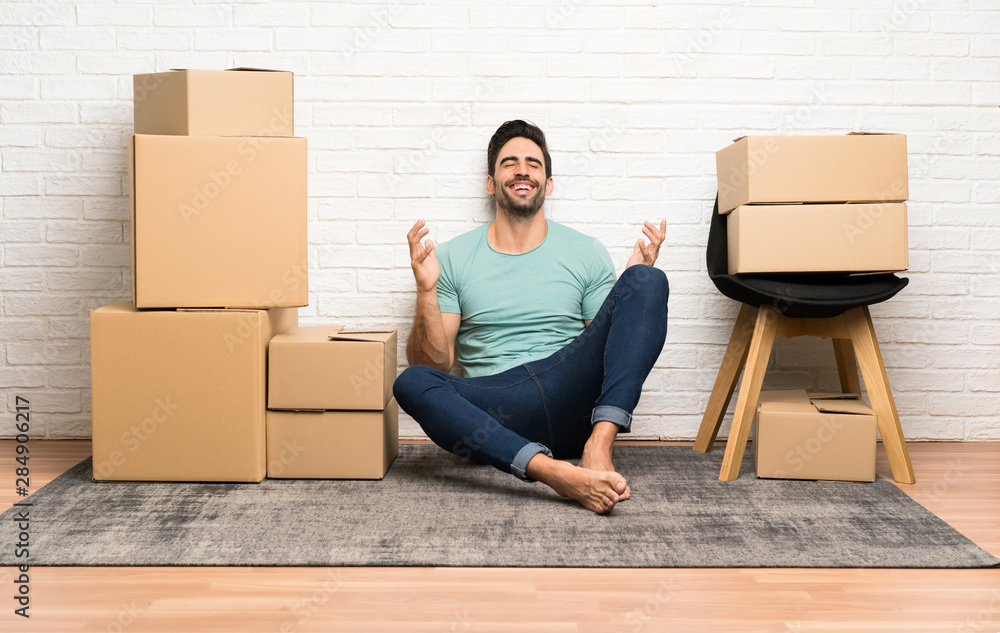 Handsome young man moving in new home among boxes laughing Handsome young man moving in new home among boxes laughing