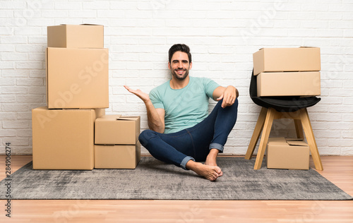 Handsome young man moving in new home among boxes holding copyspace imaginary on the palm