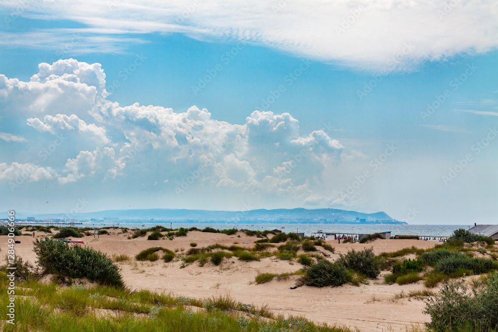 Sandy beach with sand dunes by the sea against the blue sky.