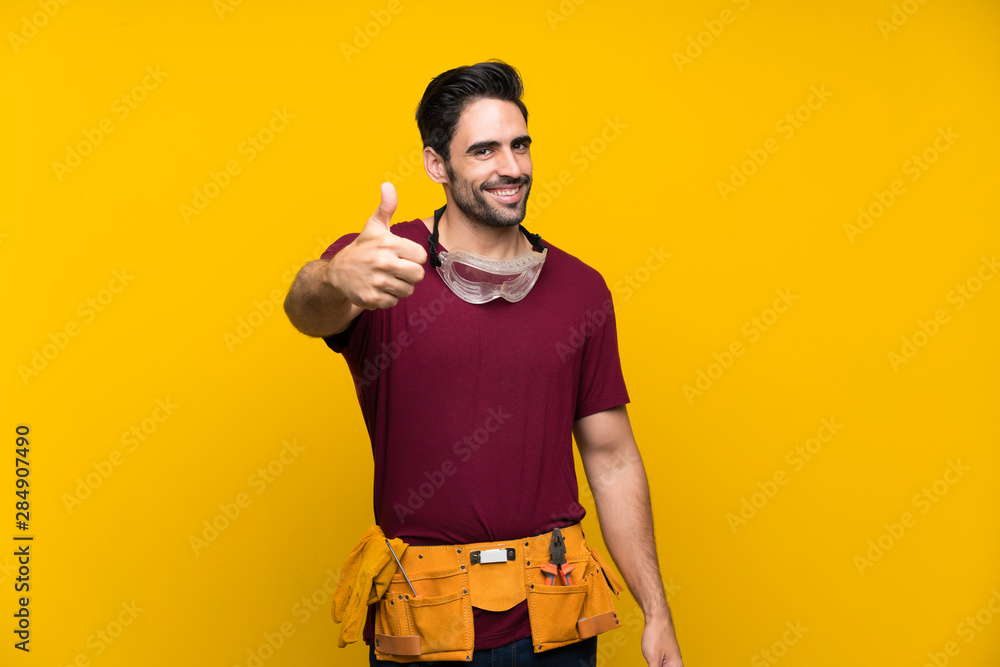 Handsome young craftsman over isolated yellow background with thumbs up because something good has happened Handsome young craftsman over isolated yellow background with thumbs up because something good has happened