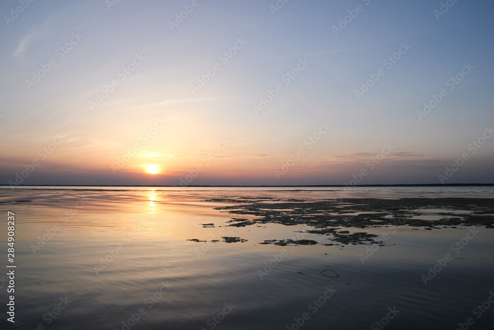 Sunset on the Dnieper river, Ukraine; landscape with sun, orange-purple sky, water and algae