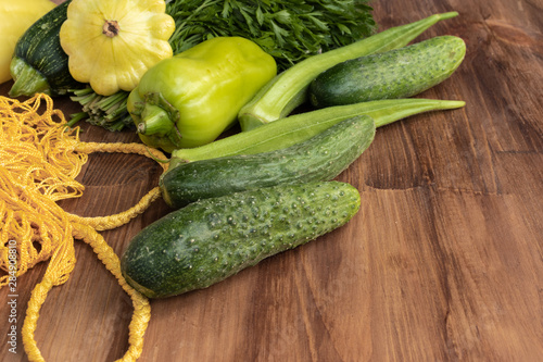 Side view of fresh green and yellow vegetables next to a yellow string bag on a brown wooden background
