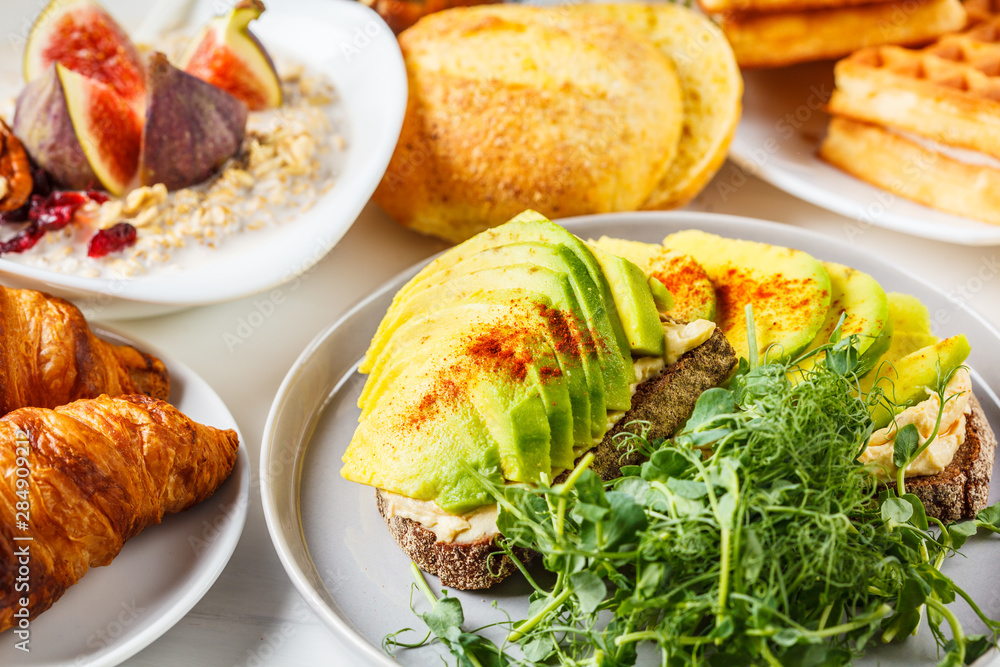 Breakfast table with avocado toast, oatmeal, waffles, croissants on white background. Breakfast table with avocado toast, oatmeal, waffles, croissants on white background.