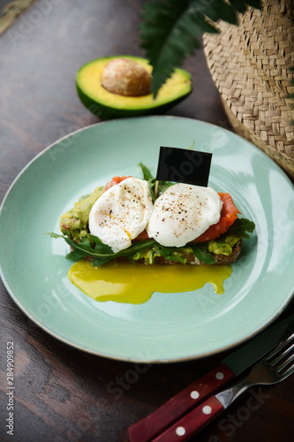 Hot toast with salmon, poached egg, herbs and avocado on a plate with a black copy space flag on a skewer