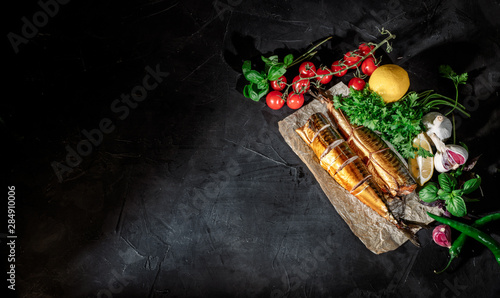 Delicious smoked fish with lemon and spices, cherry tomatoes on dark background. Top view with copy space