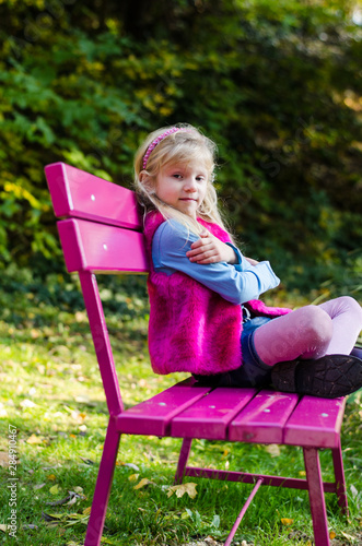 little sad child sitting in pink bench in beautiful nature
