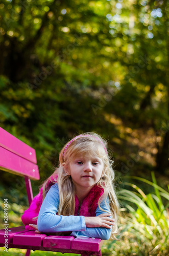 little sad child sitting in pink bench in beautiful nature © katarinagondova