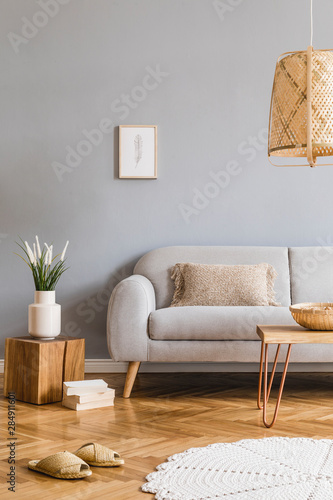 Minimalistic design home interior of living room with gray sofa, wooden coffee table, photo frame, flowers, rattan lamp, basket and elegant accessories. Stylish home decor. Template. Gray walls.