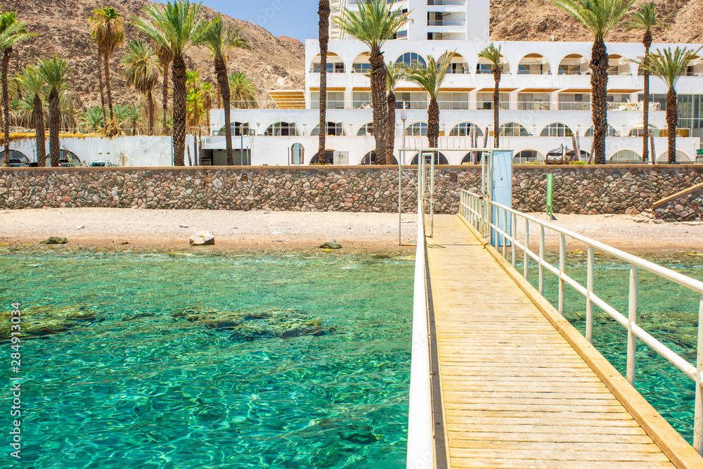 hotel resort summer vacation destination outdoor scenic view of Red sea shallow water with coral on a bottom, wooden bridge and white building apartment background 