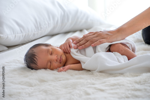 Soft blur of mother hand carefully touch her baby on white bed with bright light of day time.