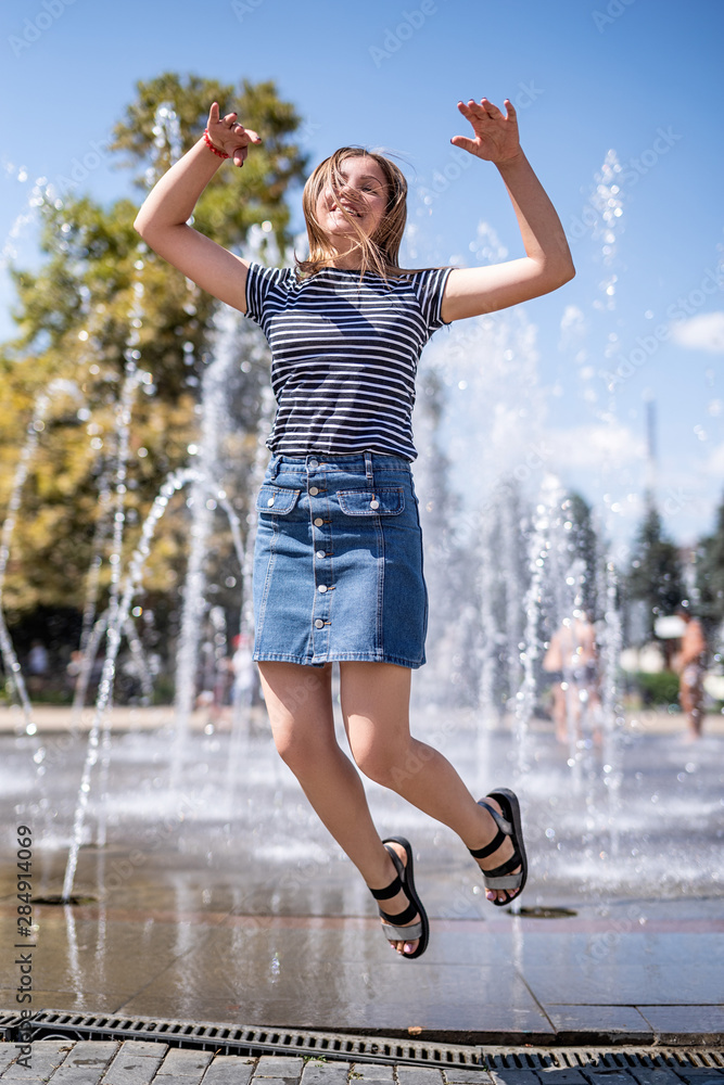 young happy attractive caucasian woman jumping and laughing near fountain in the urban park