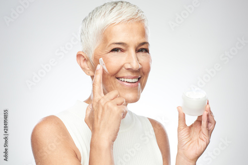 Gorgeous smiling Caucasian senior woman trying out new anti age cream and looking at camera. Beauty photography.