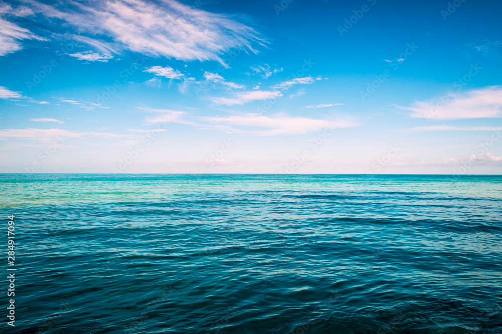 Fototapeta premium Infinite horizon with hazy white tropical clouds above bands of tropical blue empty sea