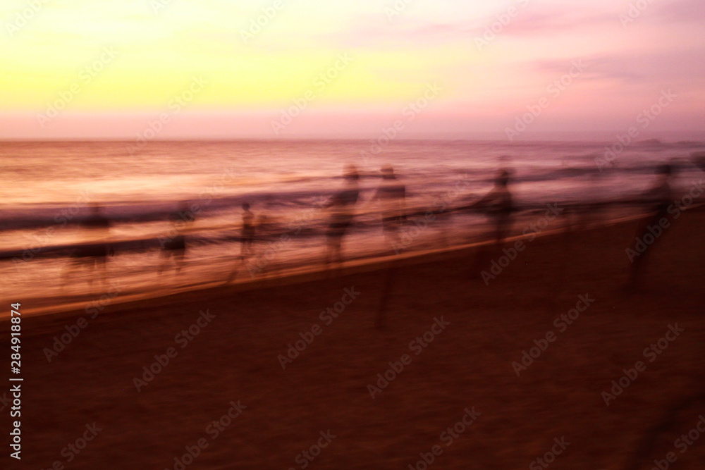 Long time exposure: Ghostly silhouettes of blurred fishermen catch up their net during sunset on beach, Sri Lanka