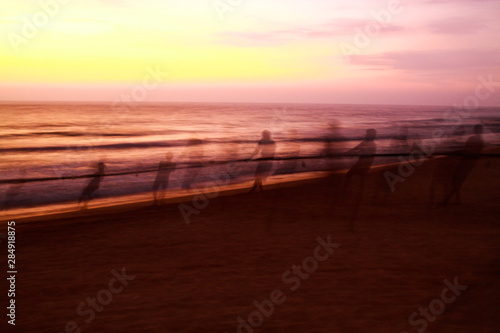 Long time exposure: Ghostly silhouettes of blurred fishermen catch up their net during sunset on beach, Sri Lanka