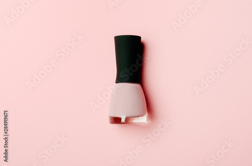 Nail polish bottle on stylish pink background. Pink fingernail varnish with black cap. Female cosmetics accessory. Manicure enamel, pedicure lacquer top view on nude backdrop. Minimalist promo banner © mellisandra
