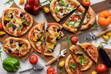 Flat lay of vegetarian pizzas. Freshly made big and small pizzas with eggplants, bell peppers, tomatoes, olives and basil on white background