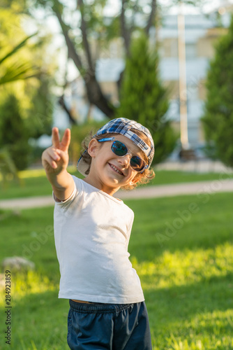 Portrait of a boy with cap and sunglasses gesturing.