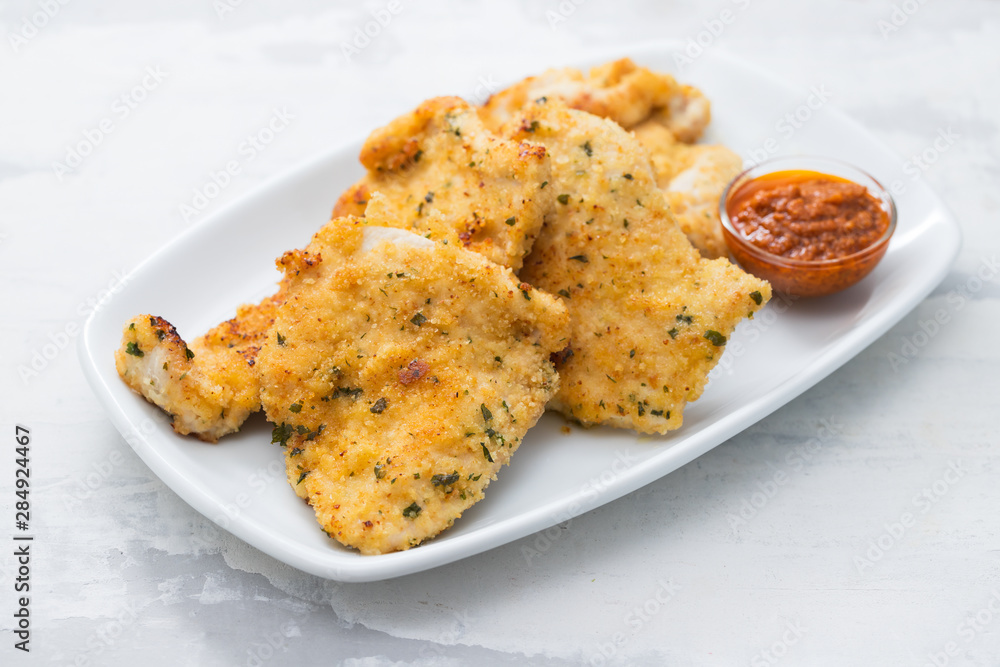 fried chicken breast with sauce on white dish on ceramic background fried chicken breast with sauce on white dish on ceramic background