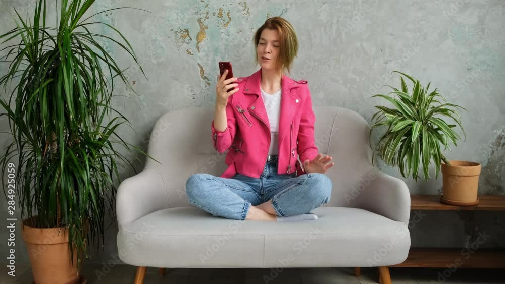 Young hipster millenial woman makes a video call and uses a mobile phone in a modern ecological loft interior. Green home plants. Young hipster millenial woman makes a video call and uses a mobile phone in a modern ecological loft interior. Green home plants.