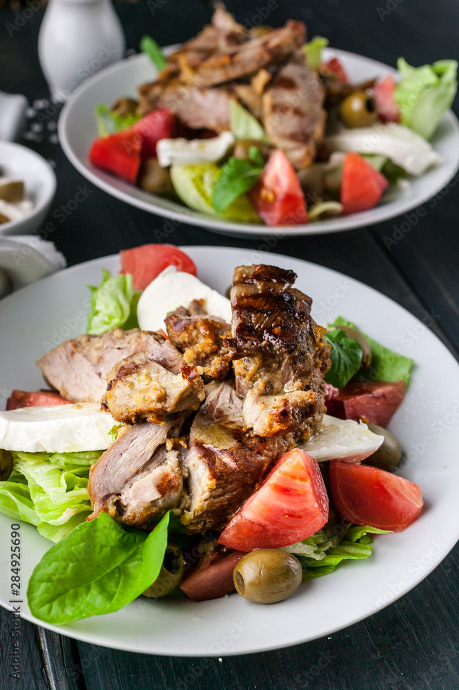 Two servings of grilled meat and salad with vegetables, mozzarella and herbs. Traditional Mediterranean Cuisine. Vertical shot Two servings of grilled meat and salad with vegetables, mozzarella and herbs. Traditional Mediterranean Cuisine. Vertical shot