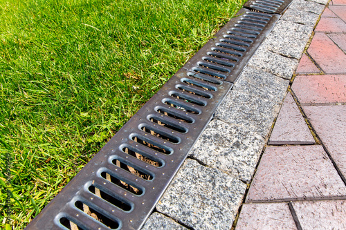 iron grate of a drainage system for storm water drainage from a pedestrian sidewalk near a green lawn. photo