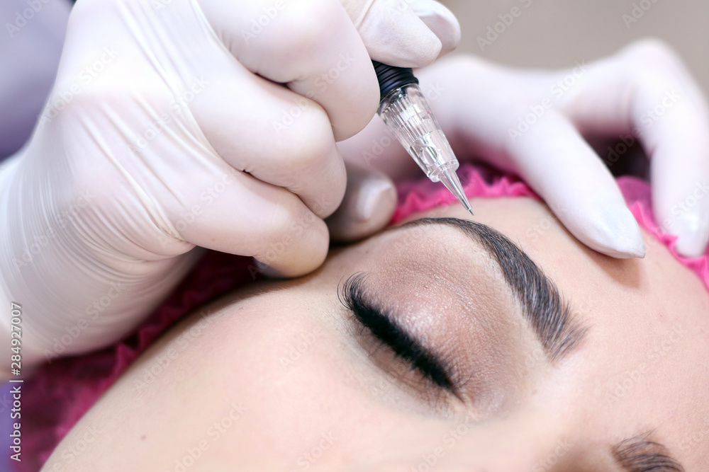  Young woman having permanent makeup on eyebrows in beautician salon