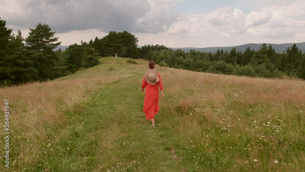 Woman walking hilltop forest road, enjoying pristine fields filled with wildflowers in a highland area - camera rise Woman walking hilltop forest road, enjoying pristine fields filled with wildflowers in a highland area - camera rise