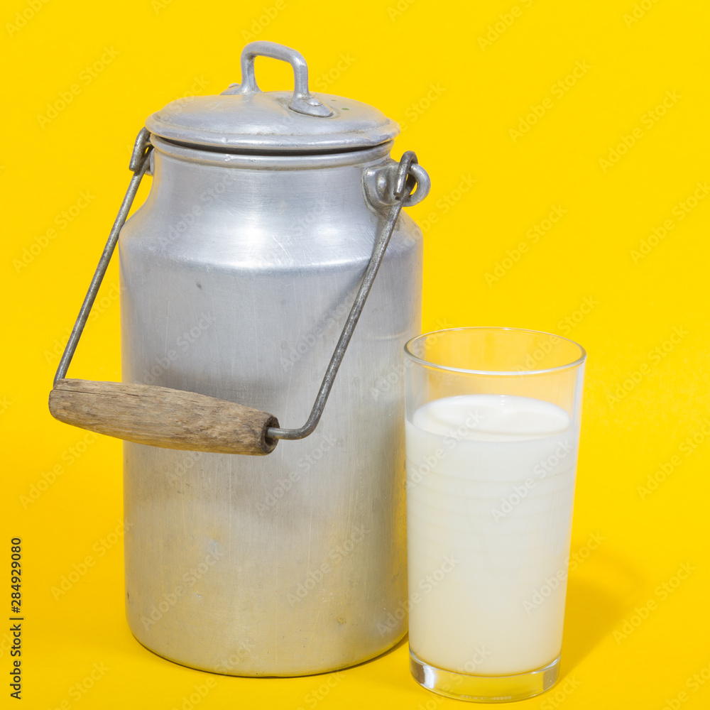 Glass of fresh milk and retro milk canister on yellow background Glass of fresh milk and retro milk canister on yellow background