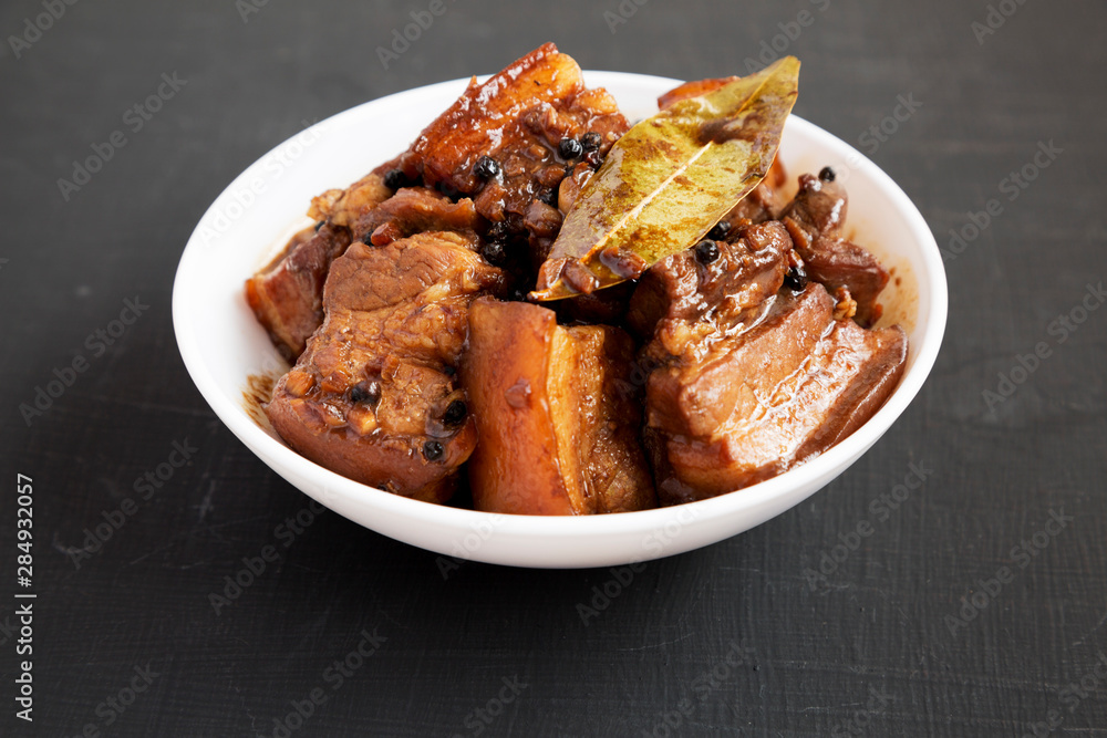 Homemade Filipino Adobo Pork in a white bowl on a black background, side view. Close-up. Homemade Filipino Adobo Pork in a white bowl on a black background, side view. Close-up.