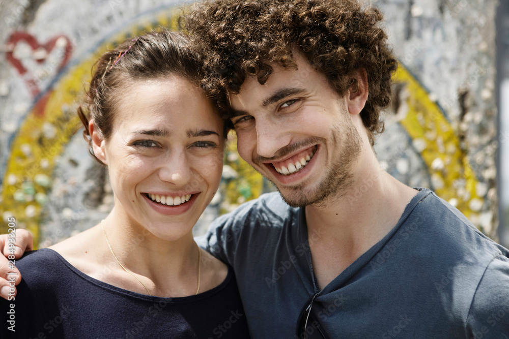 Germany, Berlin, Young couple standing in front of wall with graffiti, portrait, close-up Germany, Berlin, Young couple standing in front of wall with graffiti, portrait, close-up