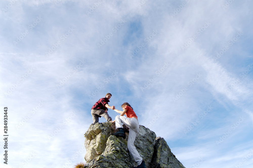 Young couple climbing on mountain peak, man helping woman, low angle view